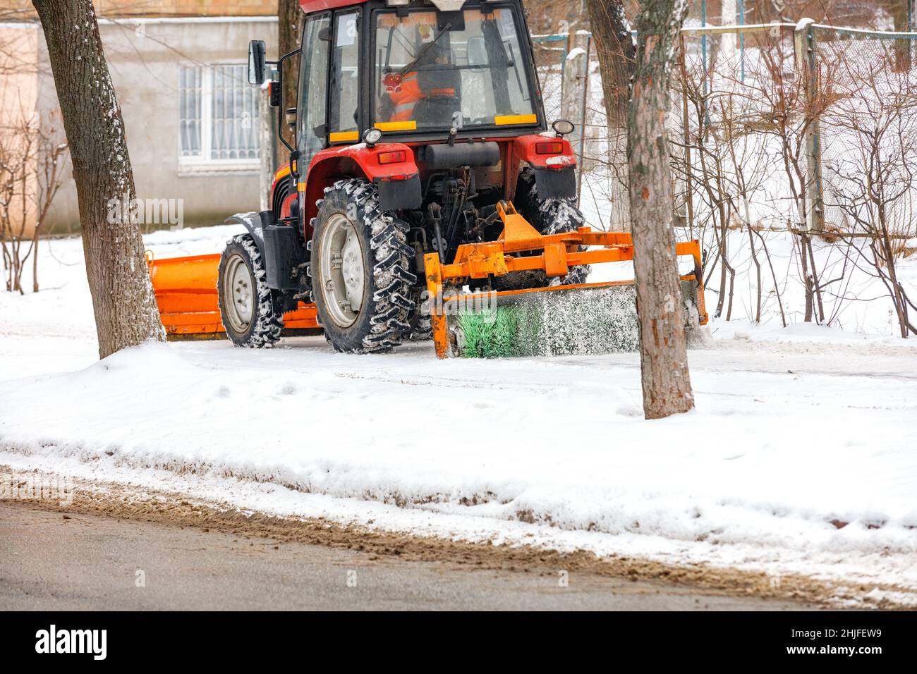 Ein kompakter Schneetraktorbläser mit Frontmesser und Bürstenschaufel schaufelt Schnee auf einem Bürgersteig der cyti Street. Speicherplatz kopieren. Stockfoto