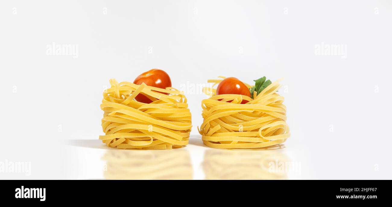 Italienische Pasta. Spaghetti Capellini, mit Kirschtomaten und Grünpflanzen, isoliert auf einem weißgrauen Hintergrund mit harten Schatten und Reflexion. Pasta in Th Stockfoto