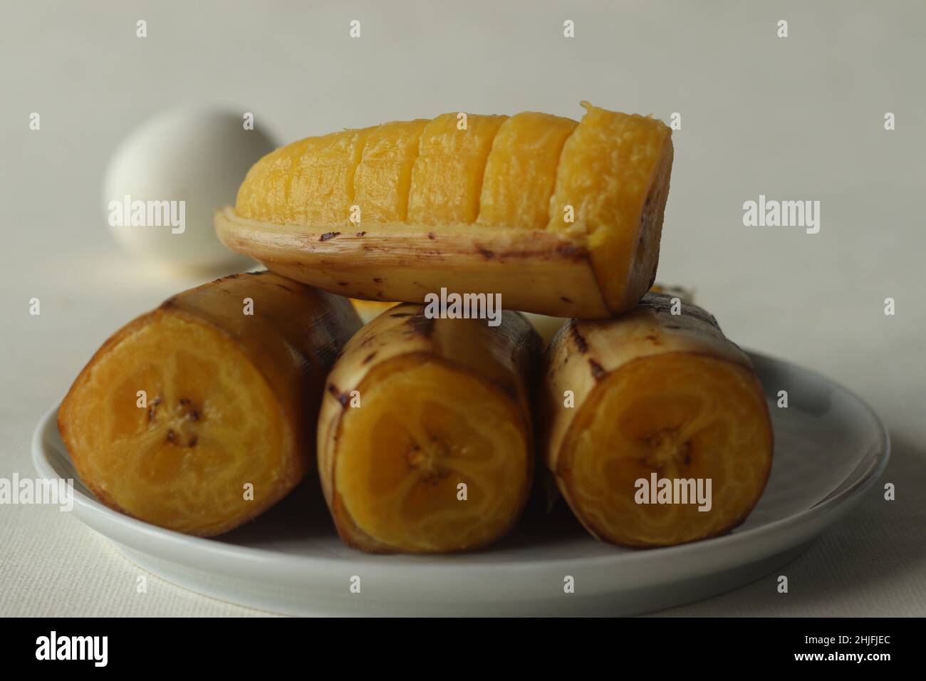 Gedämpfte Kochbanane mit gekochtem Ei im Hintergrund. Aufgenommen auf weißem Hintergrund Stockfoto