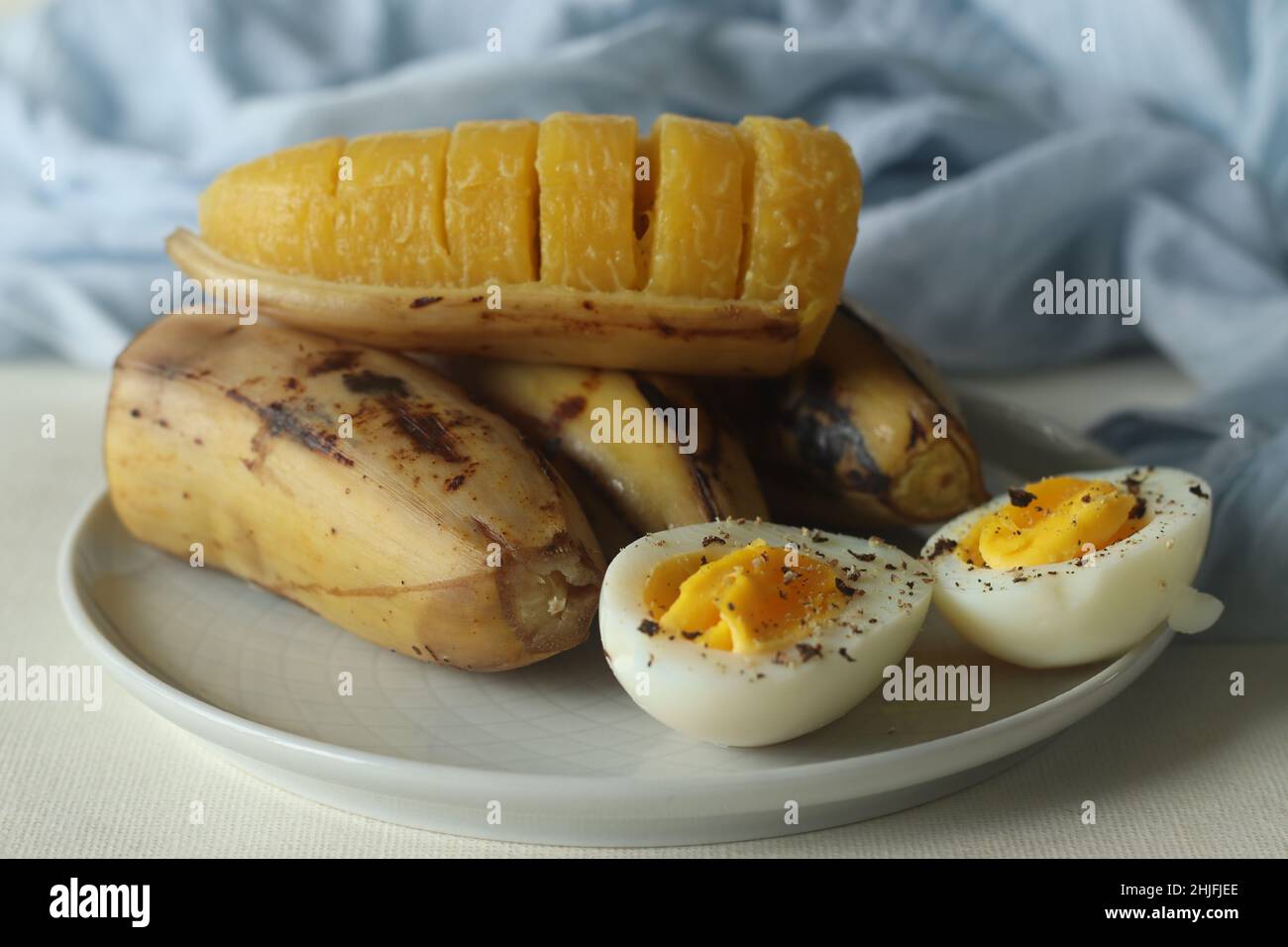 Gedämpfte Kochbanane und halbgeschnittenes gekochtes Ei mit zerdrücktem Pfeffer darauf. Aufgenommen auf weißem Hintergrund Stockfoto