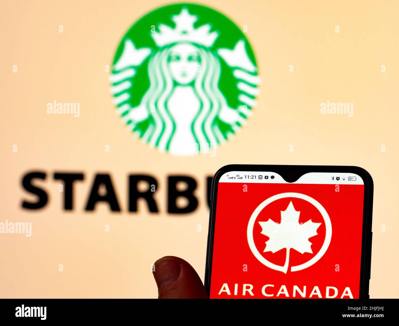 In dieser Fotobilder wird das Air Canada-Logo auf einem Smartphone-Bildschirm mit dem Starbucks-Kaffee-Logo im Hintergrund angezeigt. Stockfoto
