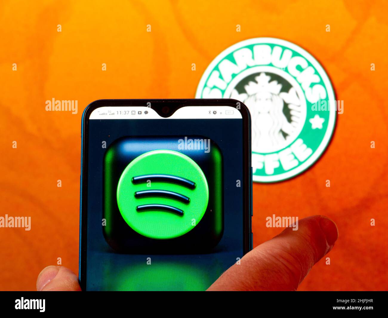 In dieser Abbildung wird das Spotify-Logo auf einem Smartphone-Bildschirm mit dem Starbucks-Kaffee-Logo im Hintergrund angezeigt. Stockfoto