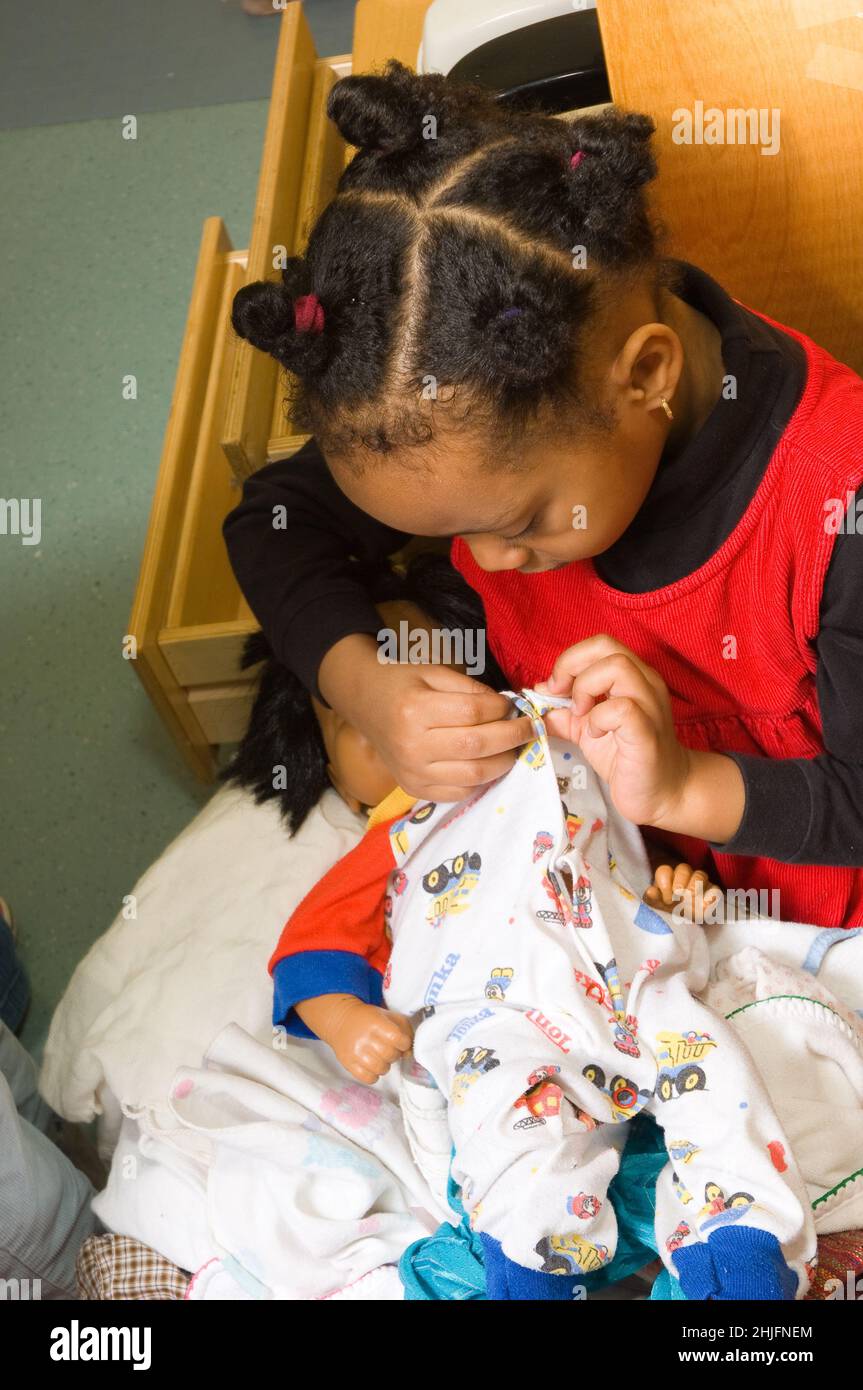 Bildung Vorschule Klassenzimmer 3-4-jährige Mädchen Befestigung Schnappschüsse auf Baby Puppe Outfit mit feinen motorischen Fähigkeiten Stockfoto