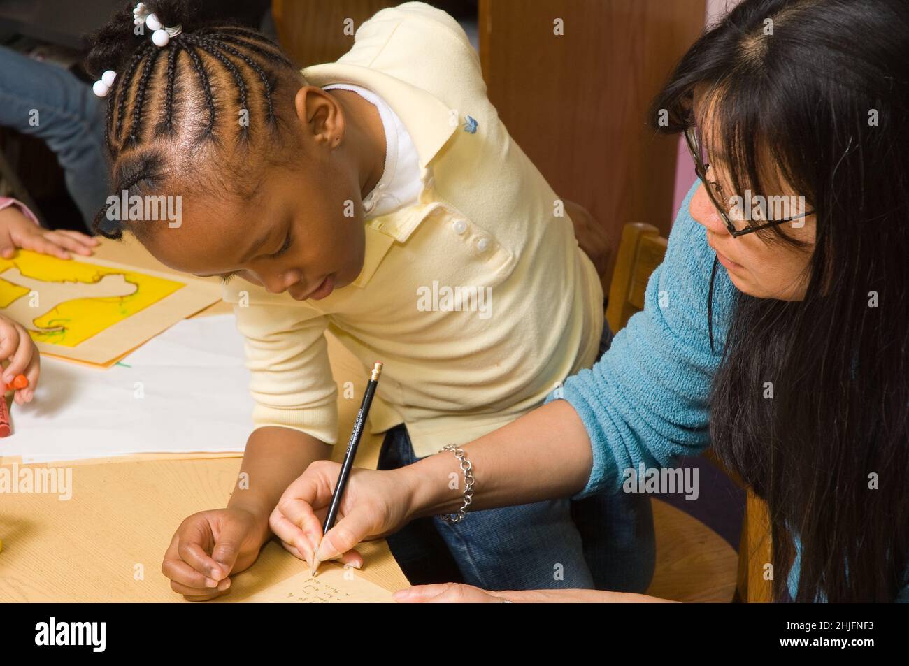 Bildung Vorschulklasse Klassenzimmer 4-5-jährige Lehrerin mit Mädchen, die aufschreiben, was das Mädchen über ihre Zeichnung sagen will Stockfoto