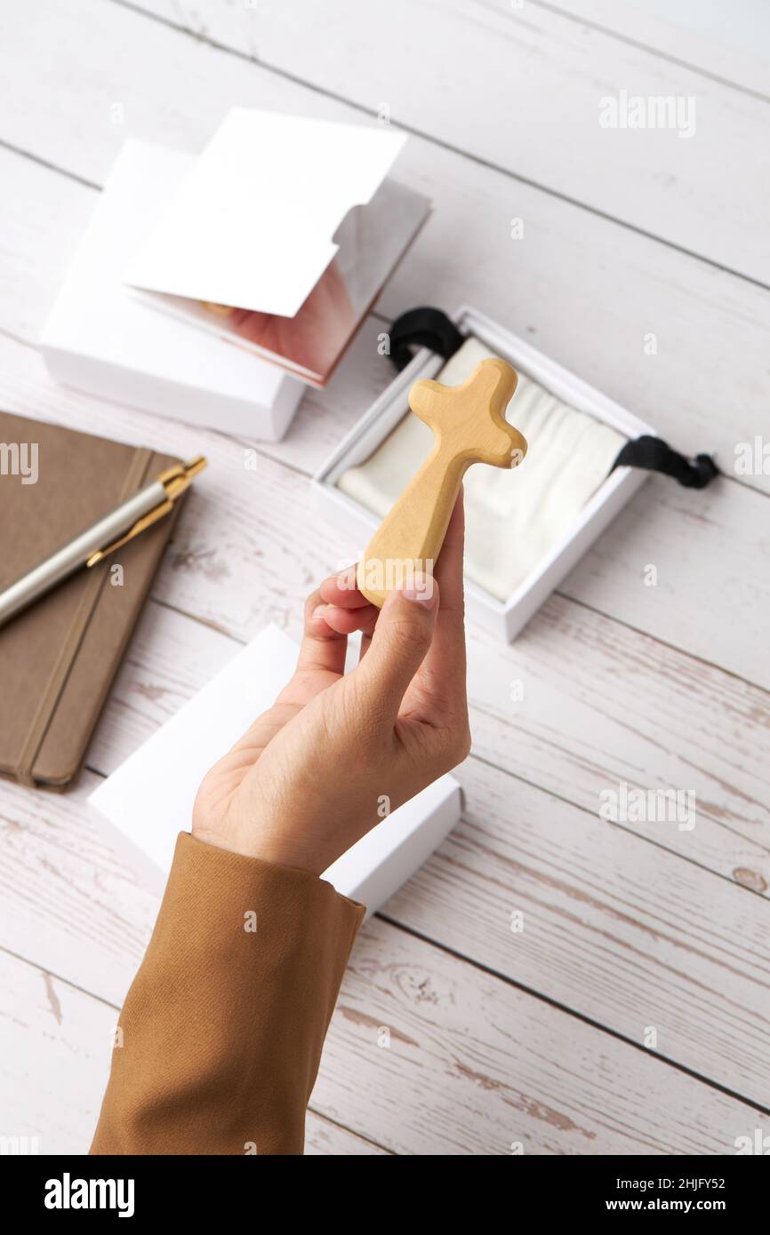 Ein Foto mit der Hand einer Person, die ein Holzkreuz hält, und anderen Dingen auf einer hölzernen Oberfläche Stockfoto