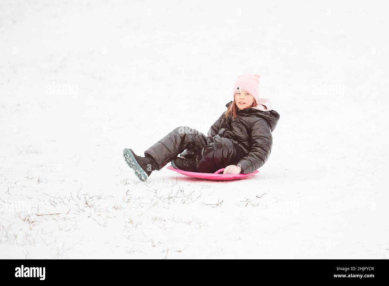 Glückliches kleines Mädchen, das auf einem Untertasse-Schlitten den Hügel hinunter rutscht. Mädchen genießen Slider Fahrt auf dem Schnee Stockfoto