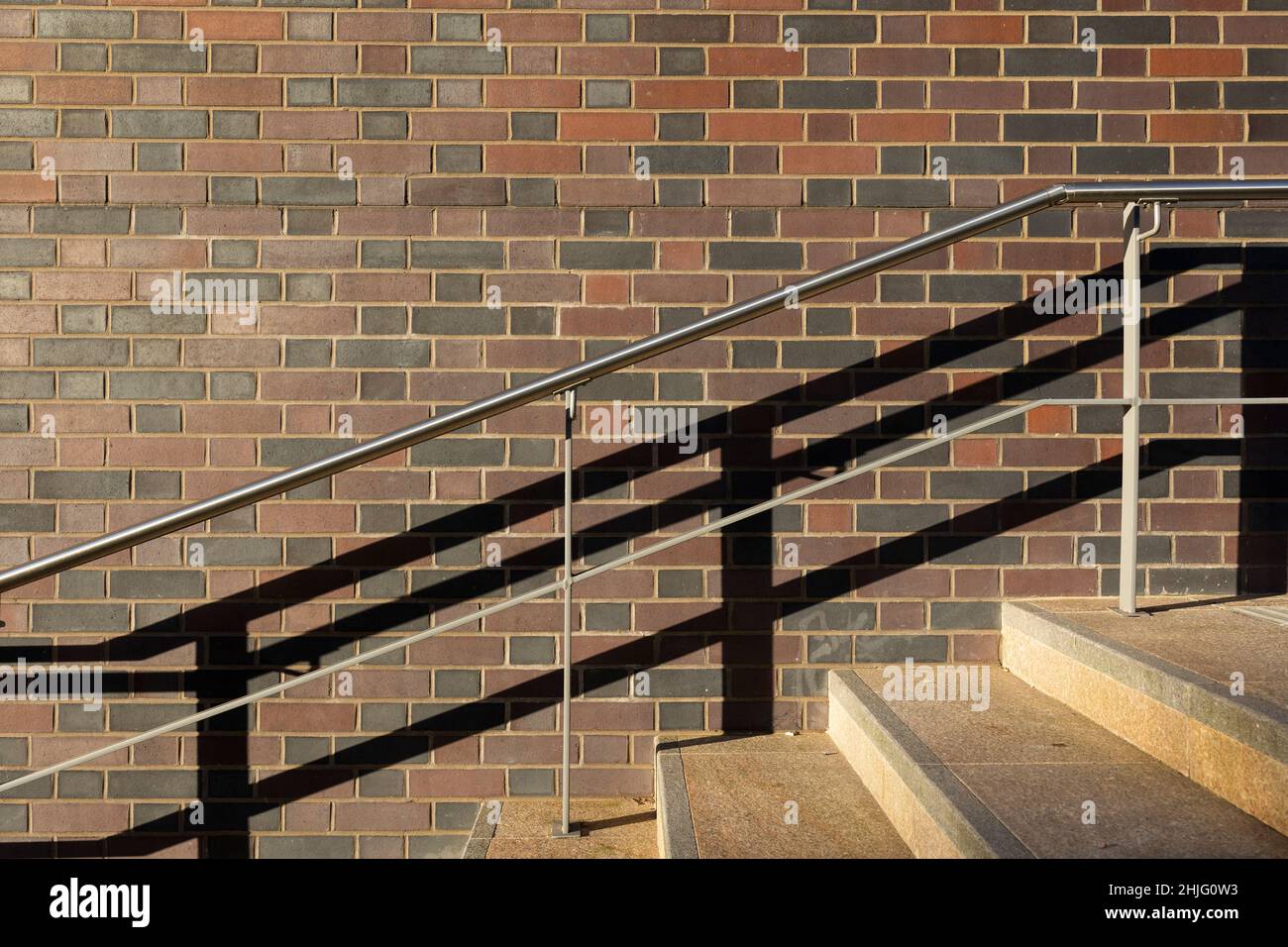 Grafische Treppengeländer und Schatten gegen eine Ziegelwand richten das Licht keiner Menschen aus Stockfoto