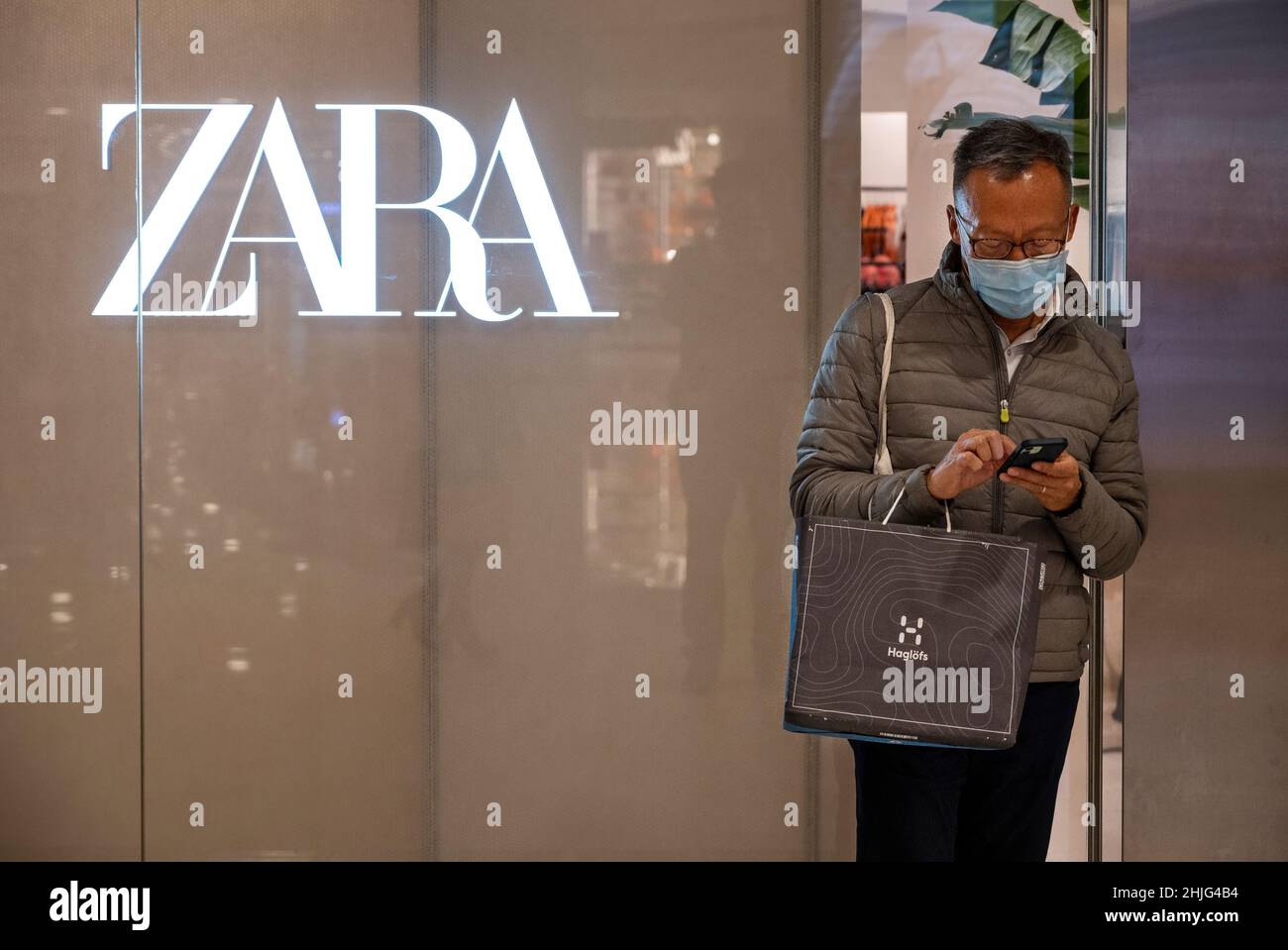 Ein Shopper nutzt ein Smartphone neben dem spanischen multinationalen Bekleidungsdesign-Einzelhandelsunternehmen von Inditex, dem Zara-Laden und -Logo in Hongkong. Stockfoto