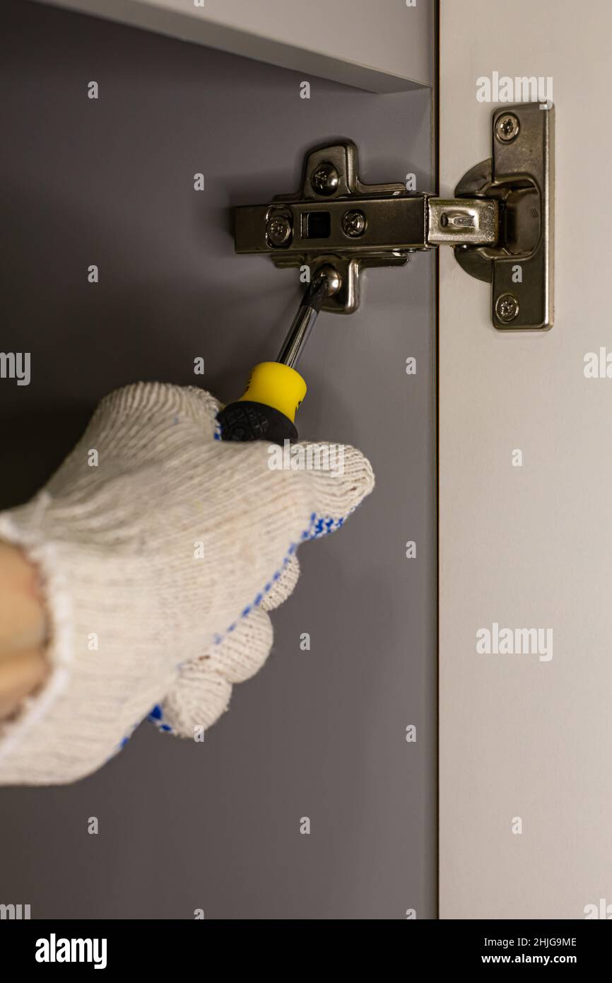 Handschlitz, der ein Scharnier der Schranktür mit einem Schraubendreher verschraubt. Hochwertige Fotos Stockfoto