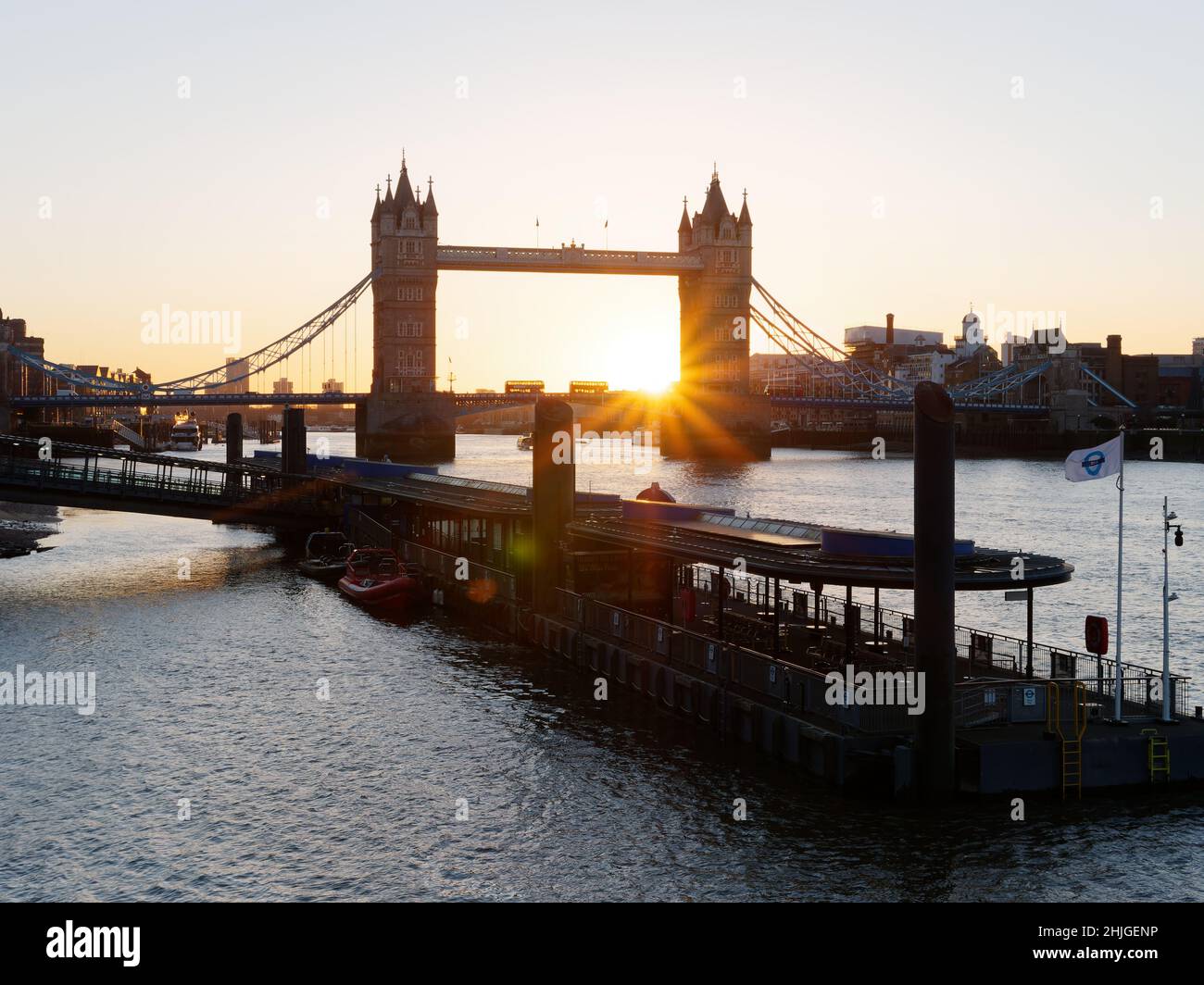 Zwei Busse überqueren die Tower Bridge an einem Wintermorgen bei Sonnenaufgang mit einem Pier an der Themse im Vordergrund, London. Stockfoto