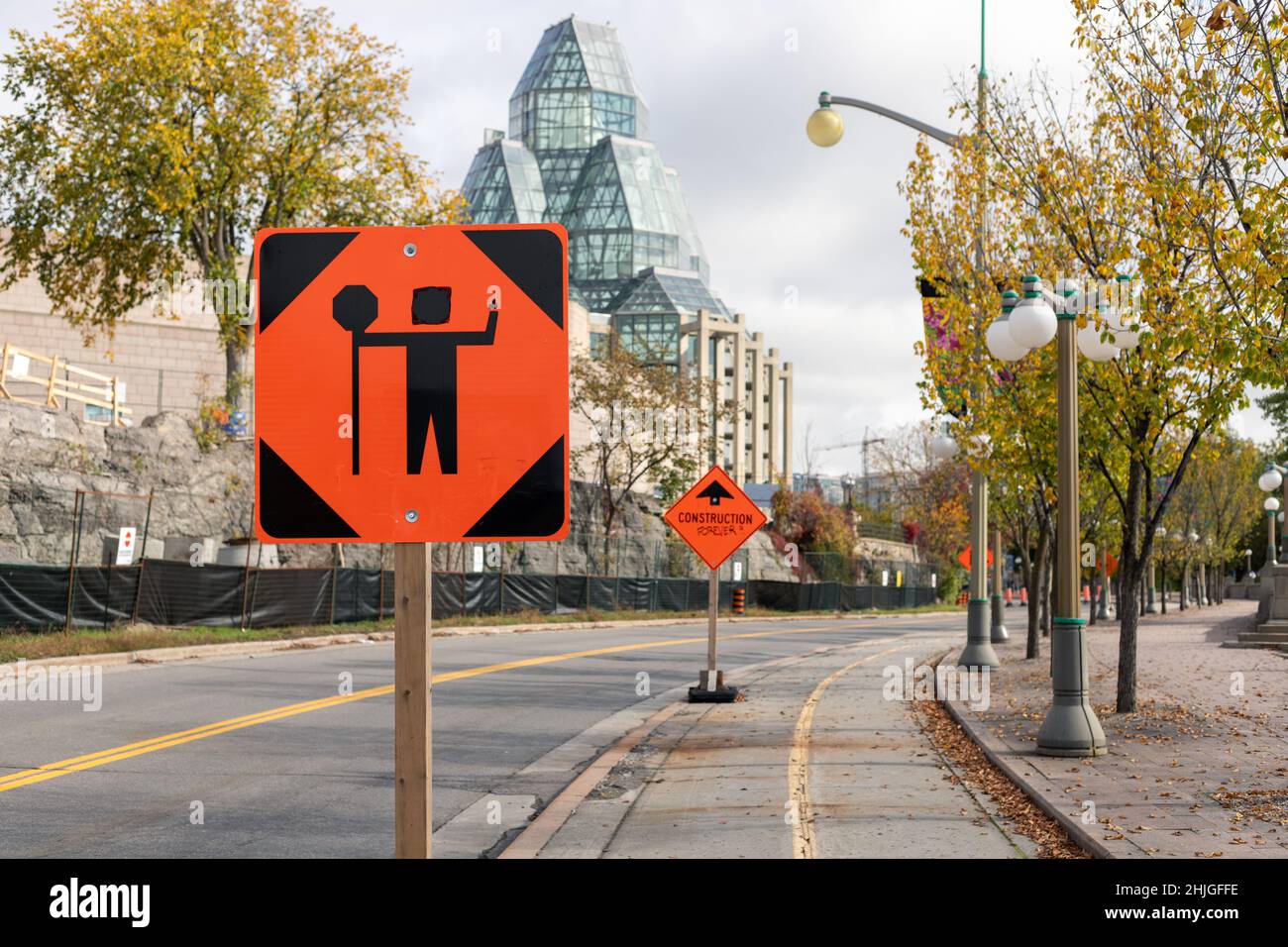 Ottawa, Kanada - 14. Oktober 2021: Verkehrskontrollperson vor dem Schild wegen Bauarbeiten in der Innenstadt der Stadt. Orangefarbenes Warnschild auf dem Stockfoto
