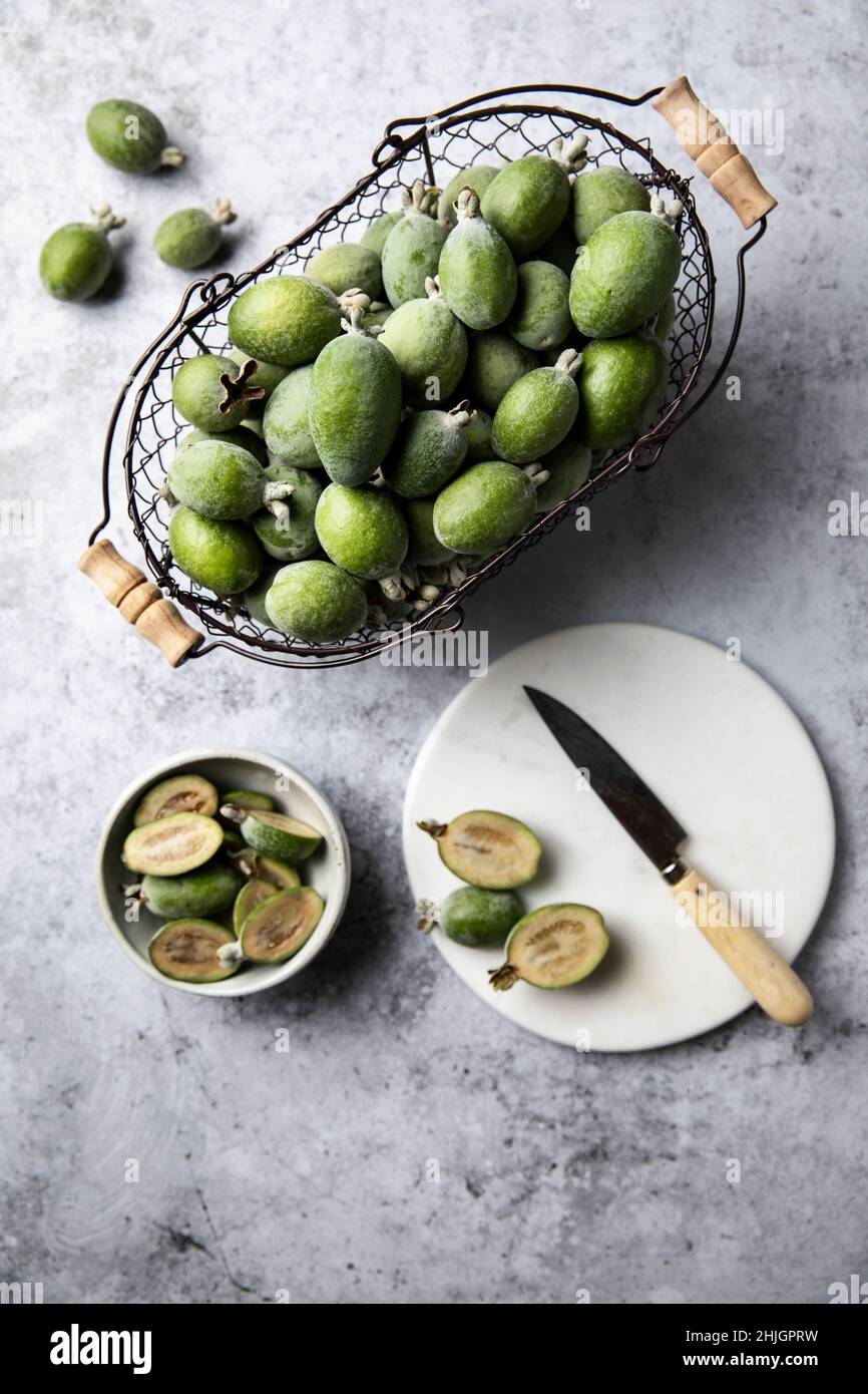 Ein Blick von oben auf einen Korb mit frisch gepflückten Feijoa-Früchten und Früchten, die auf einem Schneidebrett geschnitten wurden Stockfoto