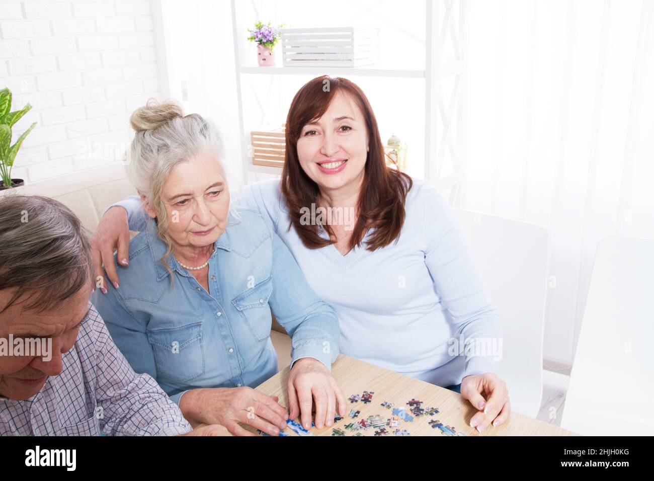 Tochter umarmt ihre ältere Mutter zu Hause für ein Puzzle-Spiel Selective Focus Stockfoto