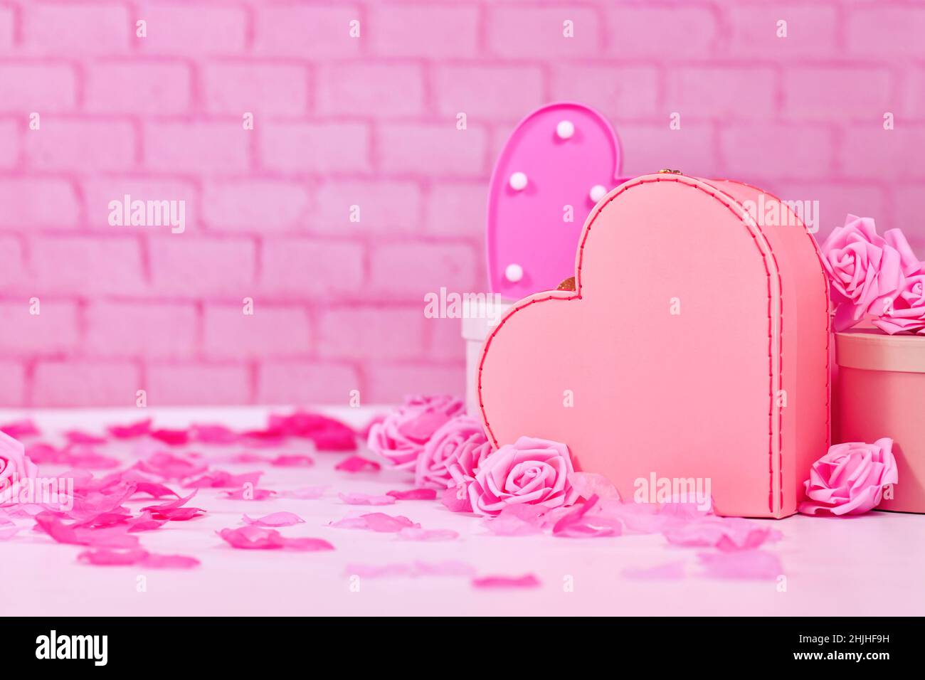 Valentinstag Komposition mit rosa Rosen, Blütenblättern, herzförmigen Geschenk-Box vor der Backsteinwand mit Kopierraum Stockfoto