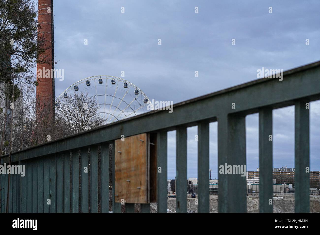 Ein Metallzaun blockiert eine Baustelle im Münchner Werksviertel. Im Hintergrund das Umadum Ferris Rad, links ein Kamin. Stockfoto