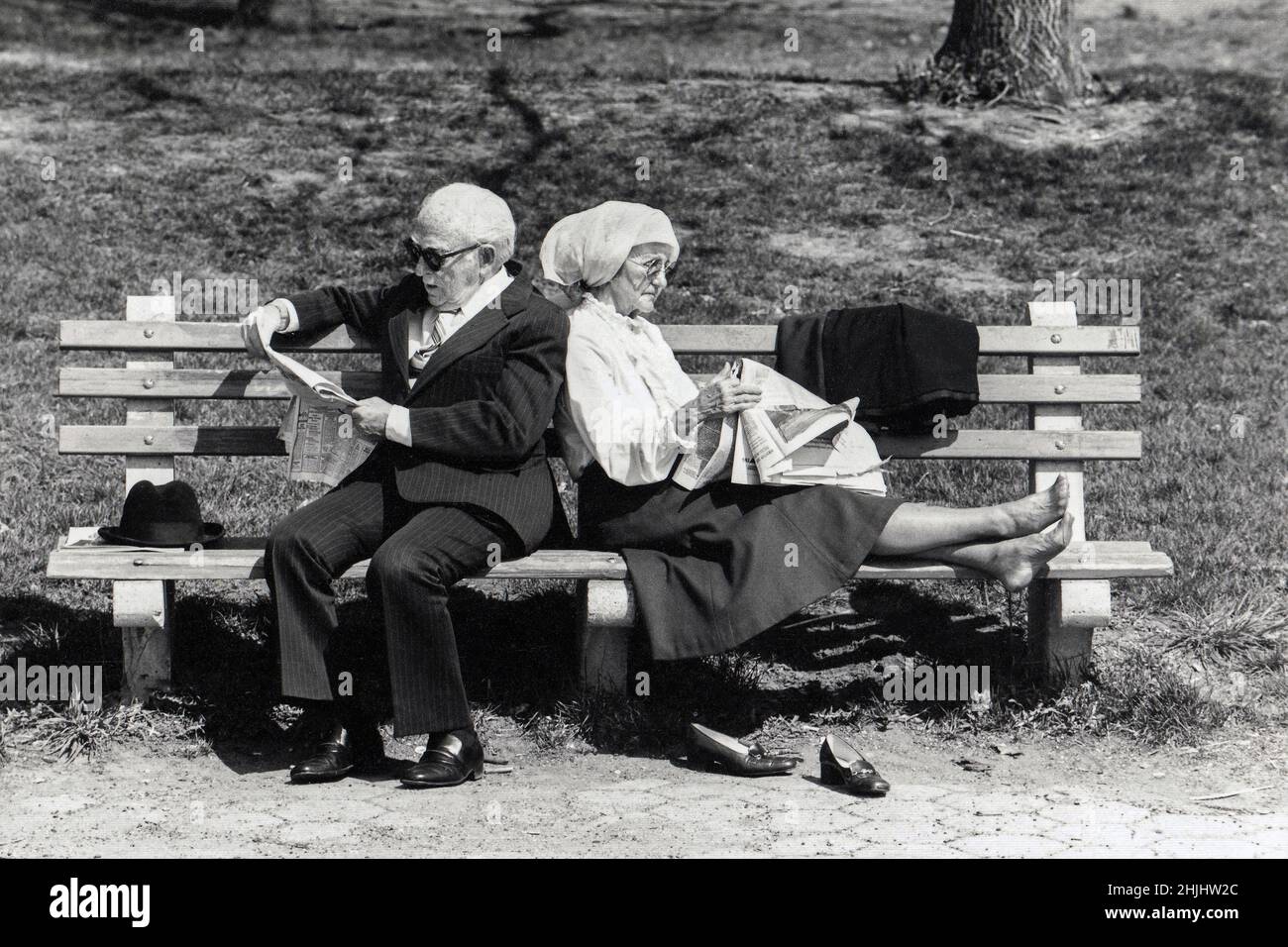 Ein älteres Paar, das sich auf einer Bank zurücklehnen und die New York Times lesen konnte. In Prospect Park, Brooklyn, New York. Ca. 1975. Stockfoto
