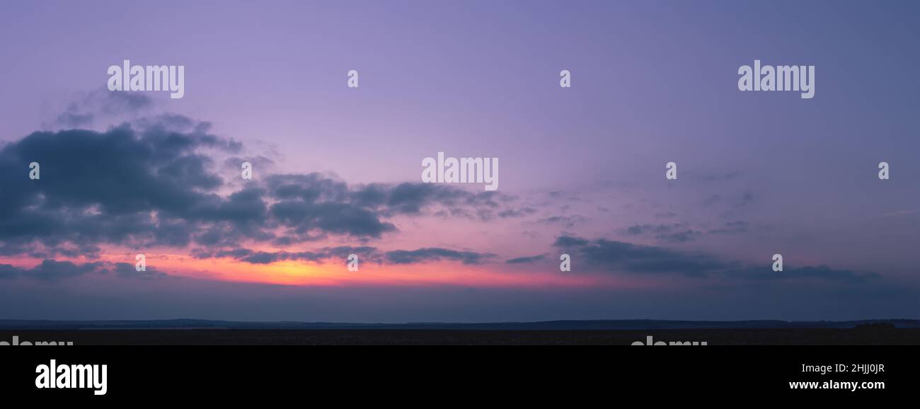 Lila Sonnenuntergang mit der Sonne hinter den Wolken. Farbenprächtiger, wolkiger Himmel bei Sonnenuntergang. Verlaufsfarbe. Himmel Textur, abstrakte Natur Hintergrund Stockfoto