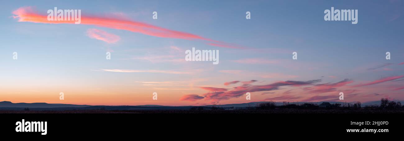 Panorama des dramatischen bunten Sonnenuntergangs mit dunklen und hellen Wolken. Die Sonnenstrahlen brechen durch den wolkigen Himmel. Dunkle Wolken gegen einen hellen Tisch Stockfoto