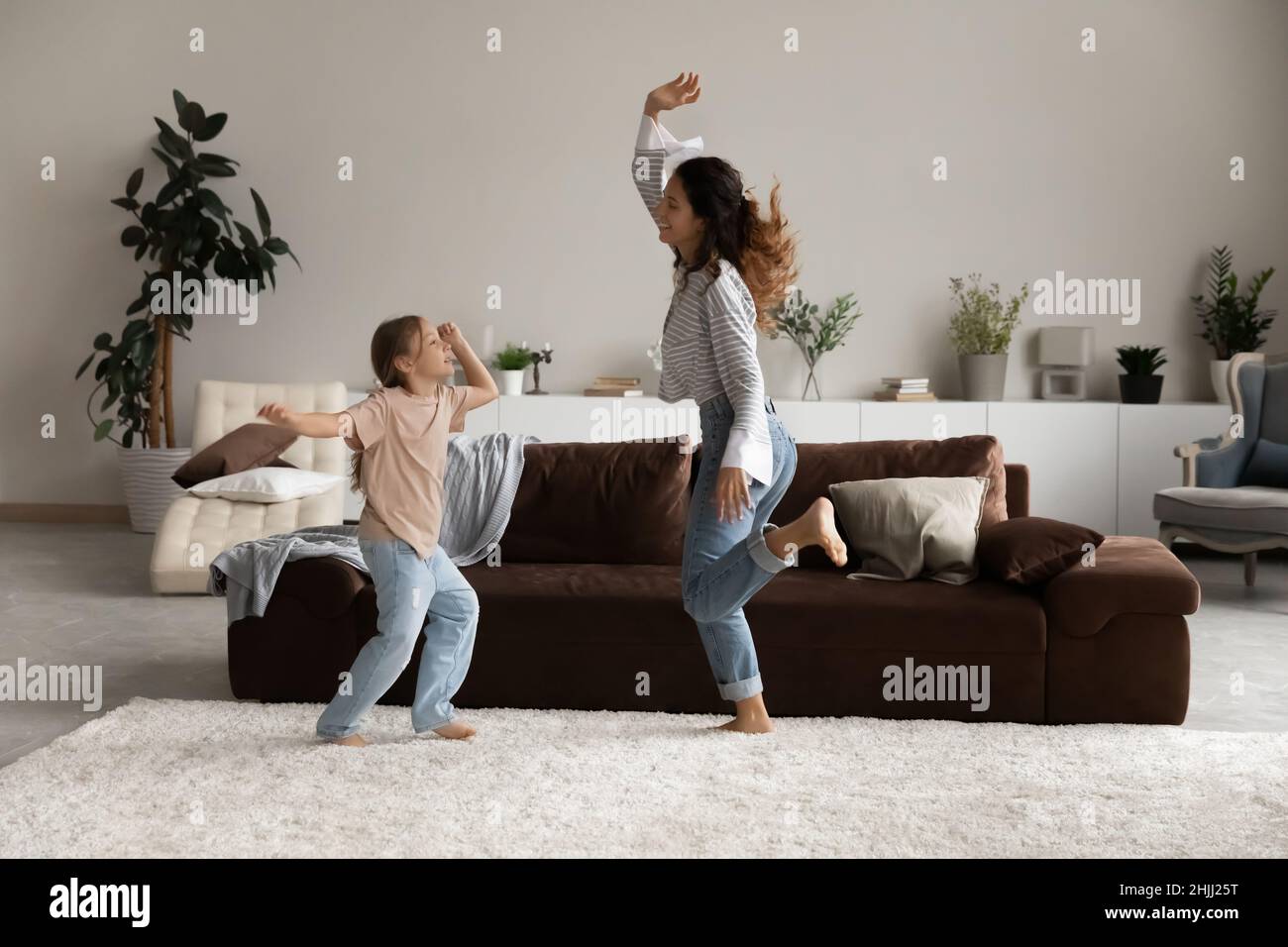 Fröhliche Frau, ihre kleine Tochter, die im Wohnzimmer tanzt Stockfoto