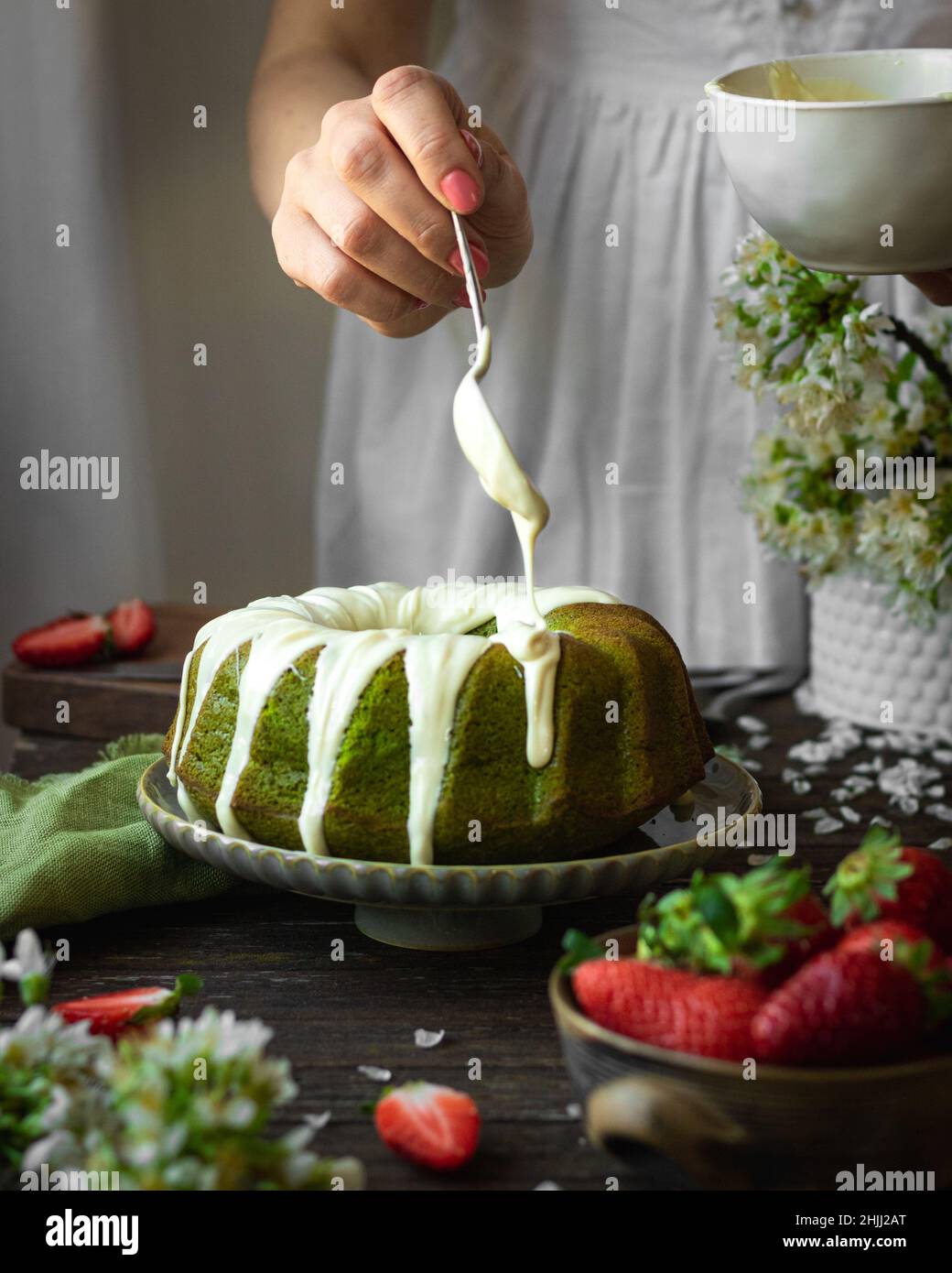 Grüner Spinat Kuchen mit Erdbeere auf einem dunklen rustikalen Holzhintergrund. Mädchen in weißem Kleid Gießen Sahnehäubchen auf Kuchen. Frühling Stillleben Stockfoto