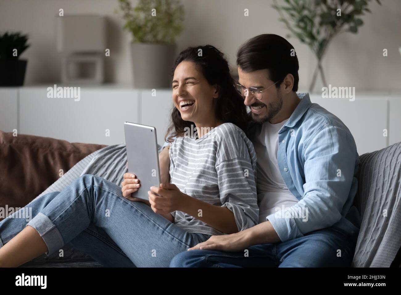 Fröhliches, lachendes Paar sitzt auf dem Sofa mit digitalem Tablet Stockfoto