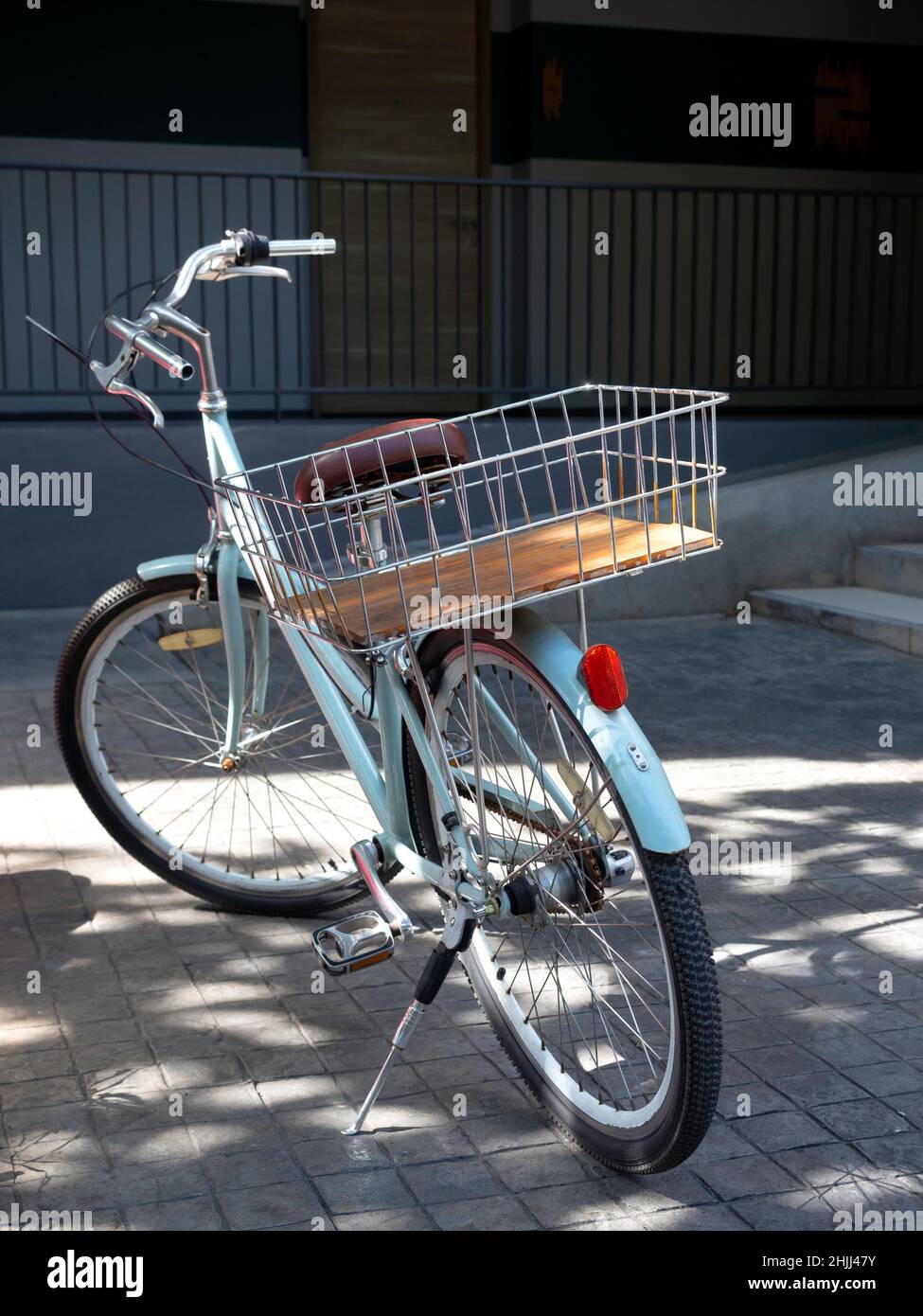 Rückansicht des blauen Vintage-Fahrrads mit Stahlkorb in der Nähe des Hotelgebäudes, Service für die Gäste, Resort-Kunde, vertikaler Stil. Stockfoto