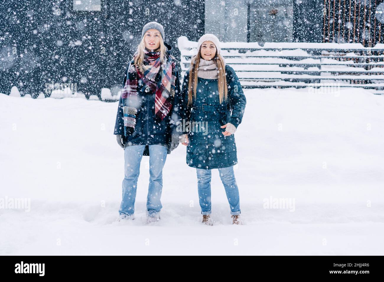 Zwei junge Frauen in warmer Winterkleidung stehen unter dem Schneefall. Stockfoto