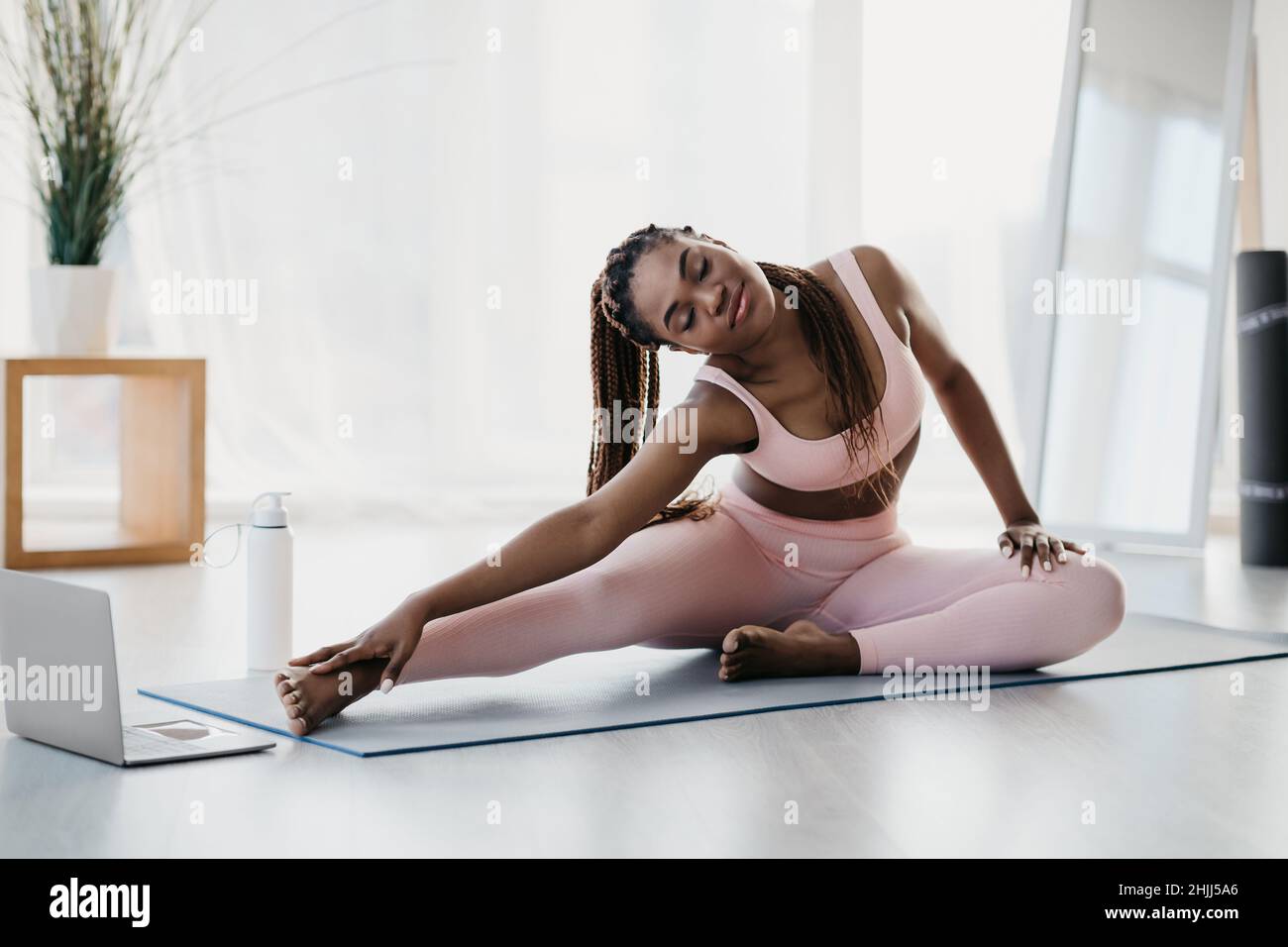 Junge schwarze Frau, die sich bei einem Heimtraining in der Nähe eines Laptops ausdehnt, Yoga praktiziert oder zu Hause Pilates praktiziert, Platz zum Kopieren Stockfoto