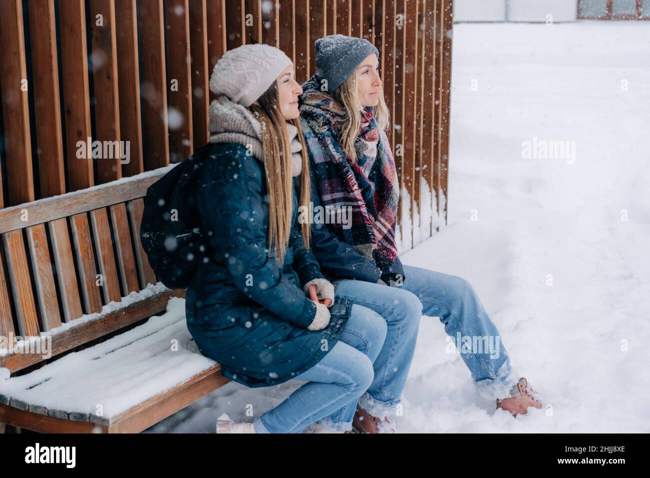 Zwei Freundinnen sitzen im Winter auf einer verschneiten Bank auf der Straße und genießen das Wetter. Stockfoto