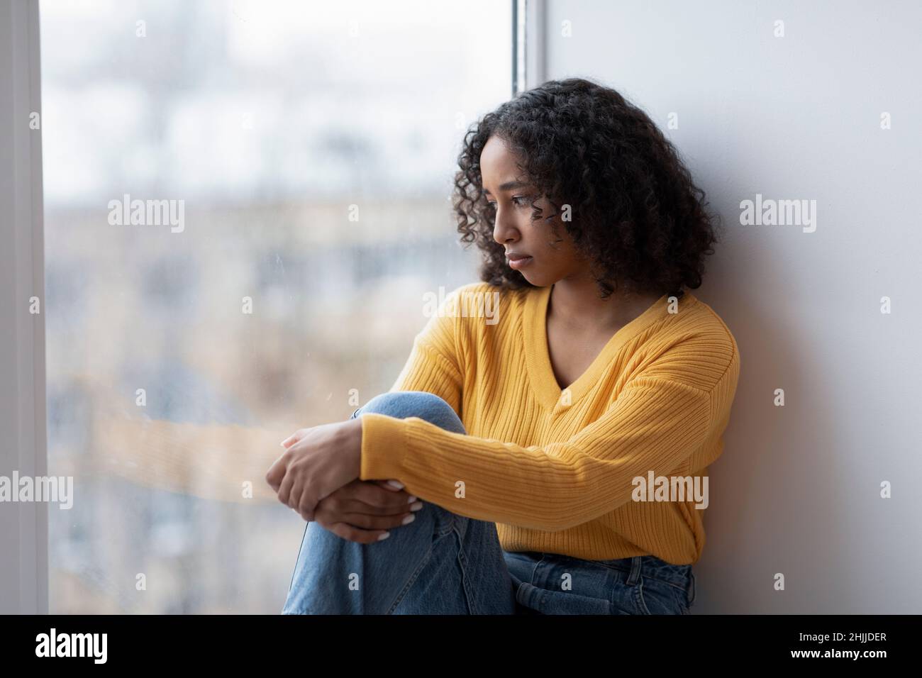 Unglückliche junge schwarze Frau, die aus dem Fenster schaut, depressive Gedanken zu Hause hat, Platz kopieren Stockfoto