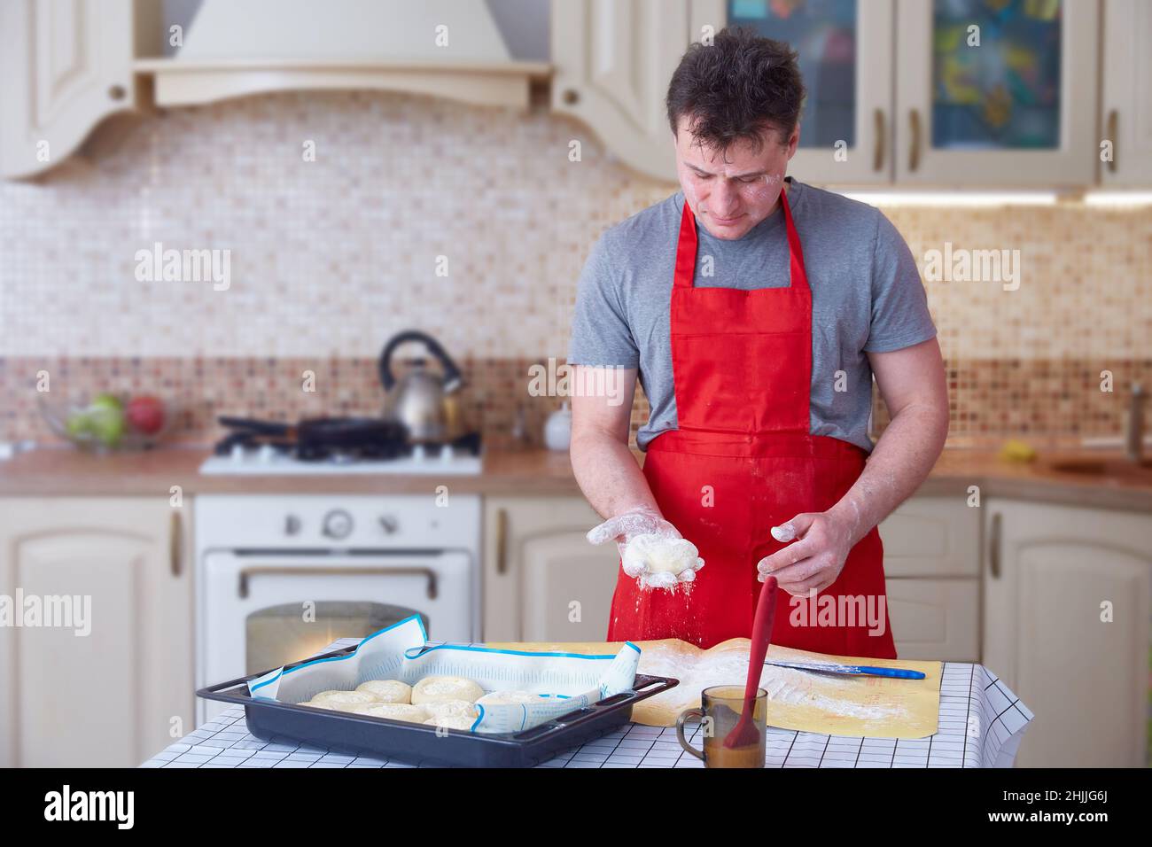 Ein Mann mittleren Alters in einer roten Schürze macht Teigkuchen zu Hause in der Küche. Lifestyle. Speicherplatz kopieren. Stockfoto