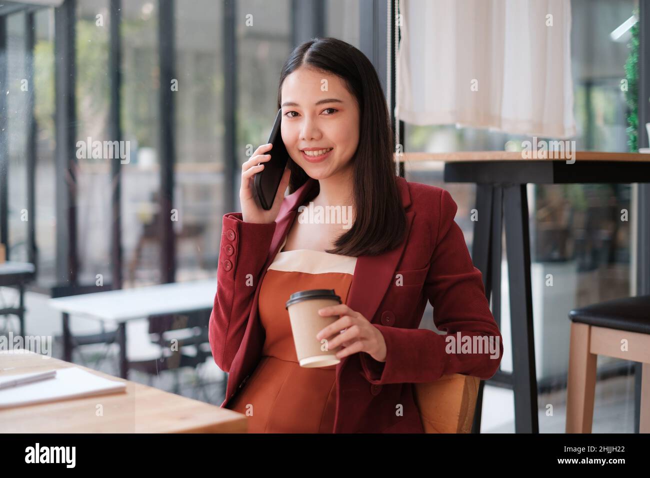 Geschäftsfrau, die mit ihrem Team über das Mobiltelefon spricht, während sie im Café erneut anspricht. Finanzierungskonzept. Stockfoto