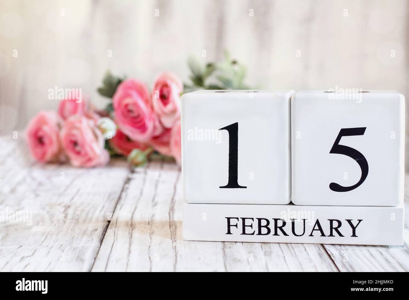 Weiße Holz-Kalenderblöcke mit dem Datum 15th. Februar für den Internationalen Tag des Krebsbewusstseins im Kindesalter. Selektiver Fokus mit rosa Ranunculus im b Stockfoto