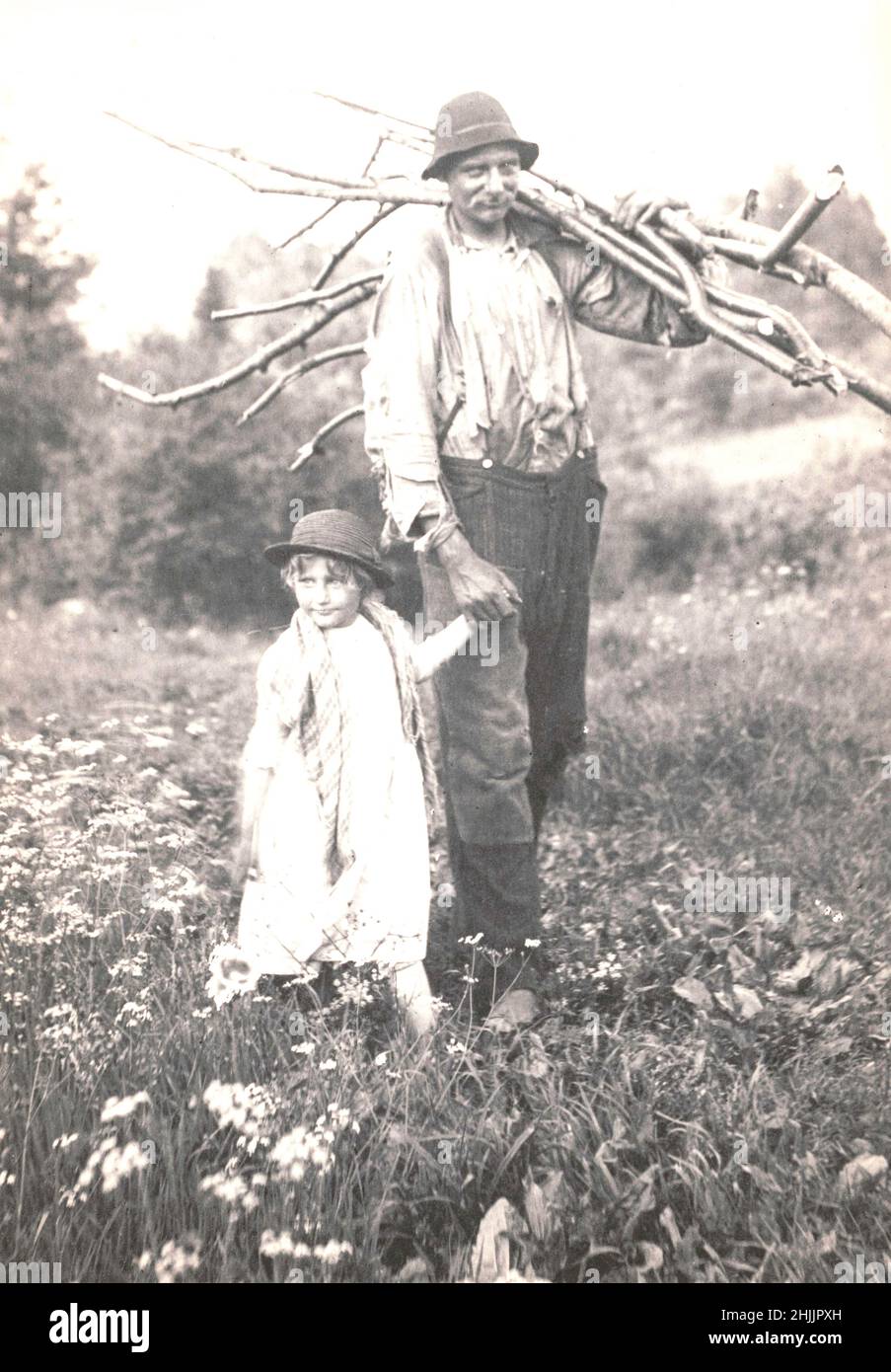 Mann, der Stöcke trägt und mit einem kleinen Mädchen auf dem Feld der wilden Blumen läuft - zwischen 1890 und 1910 Stockfoto