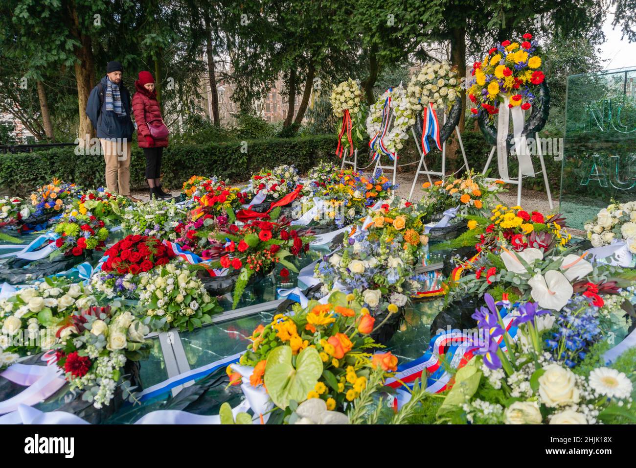 Amsterdam, Niederlande. 30. Januar 2022. Zwei Menschen betrachten die Stände mit Blumenkränzen und das Auschwitz-Denkmal der zerbrochenen Spiegel, das am Nationalen Holocaust-Gedenktag mit Blumenkränzen bedeckt ist. Kredit: Steppeland/Alamy Live Nachrichten Stockfoto