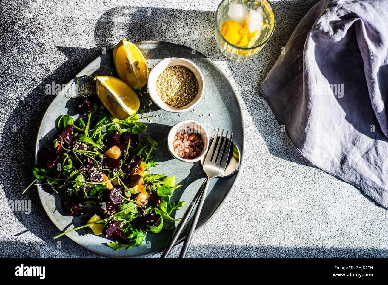 Blick von oben auf einen gegrillten Rote Beete gemischten Blattsalat mit Zitrone, Sesam und einem Glas Zitroneneiswasser Stockfoto