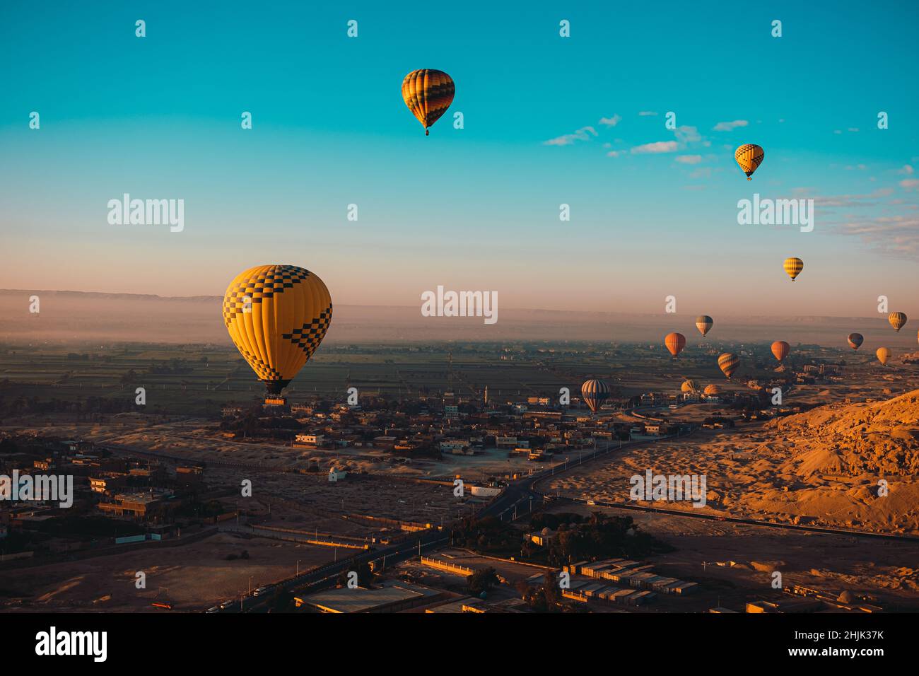 Atemberaubende vertikale Aufnahme von Dutzenden Heißluftballons, die um das luxor-gebiet in ägypten fliegen. Wüstenorangenbereich am frühen Morgen. Strahlend blauer Himmel Stockfoto