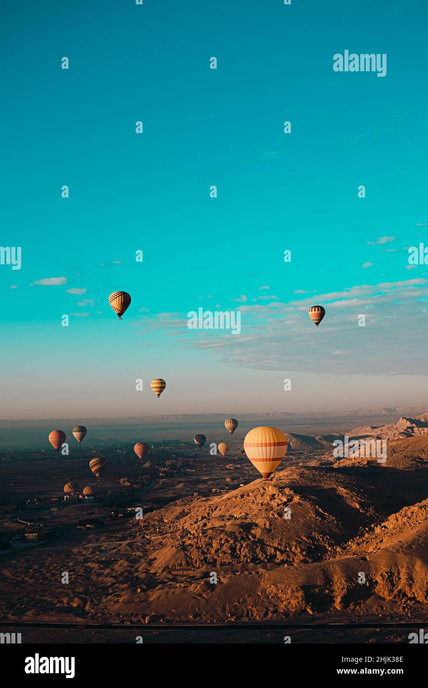 Atemberaubende vertikale Aufnahme von Dutzenden Heißluftballons, die um das luxor-gebiet in ägypten fliegen. Wüstenorangenbereich am frühen Morgen. Strahlend blauer Himmel Stockfoto