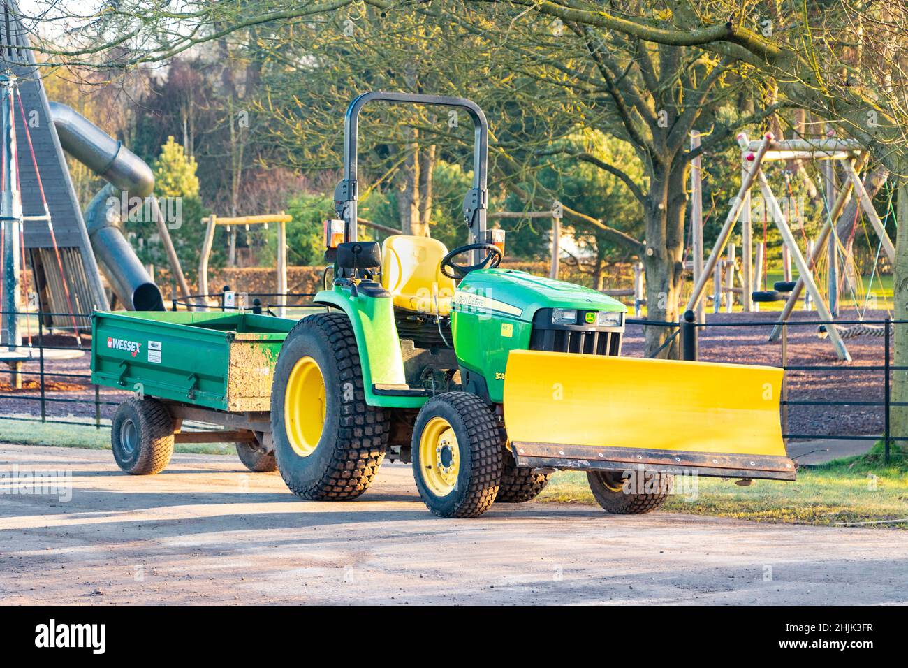 Kleiner grüner Traktor mit Klinge und Anhänger an einem kalten Wintermorgen in Trentham Gardens Stoke on Trent Stockfoto