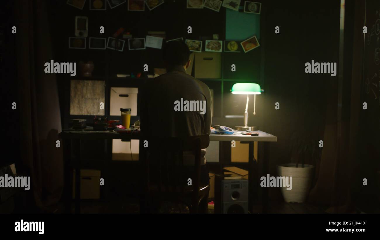 Müder junger Mann, der abends zu Hause mit einem Laptop arbeitet. Lager. Trauriger einsamer Mann, der zu Hause am Tisch sitzt. Das Konzept der Einsamkeit. Stockfoto