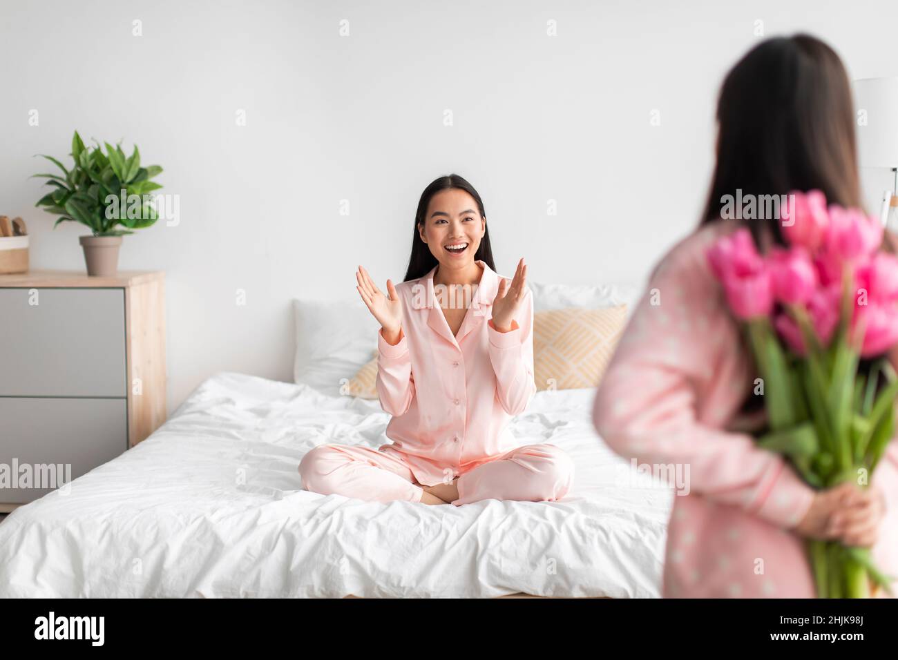 Asiatische Teenager-Mädchen mit Tulpen-Bouquet, Rücken und glücklich junge Frau auf dem Bett im Schlafzimmer innen sitzen Stockfoto