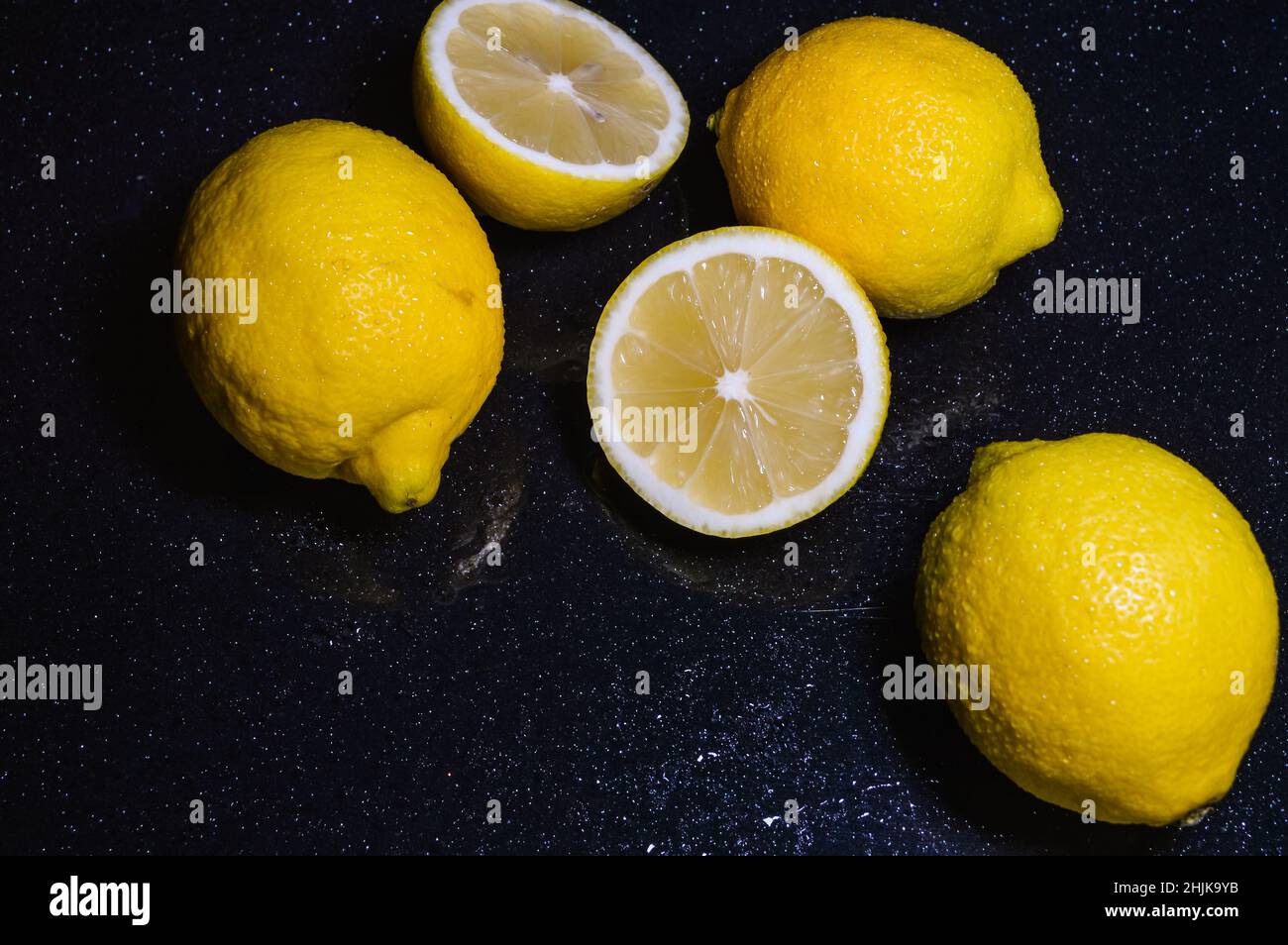 Anordnung von Halb-Zitronen und ganzen Bio-Zitronen auf einem glitzernden schwarzen Glashintergrund Stockfoto