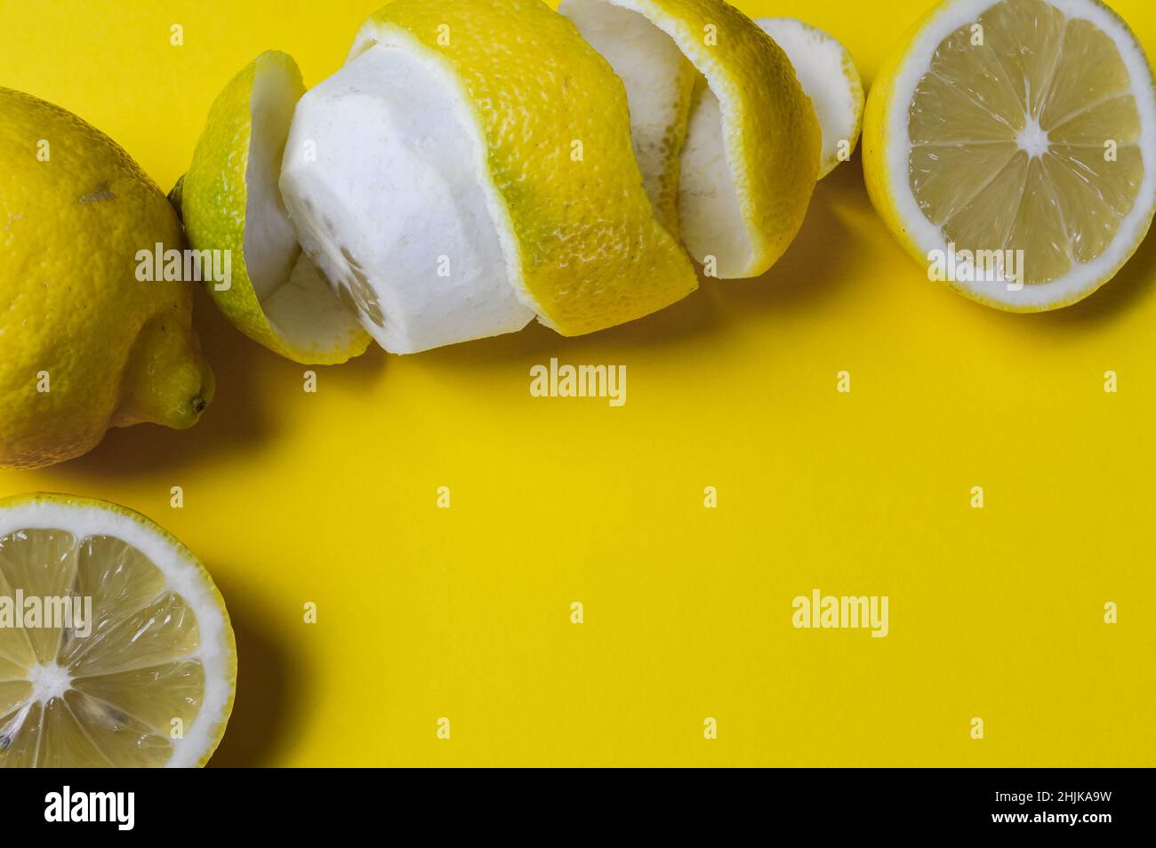 Fröhlicher Hintergrund von halbierten Zitronen und ganzen Zitronen und spiralförmiger Zitronenschale auf einem gelben Papierhintergrund mit viel Platz für etwas Text Stockfoto