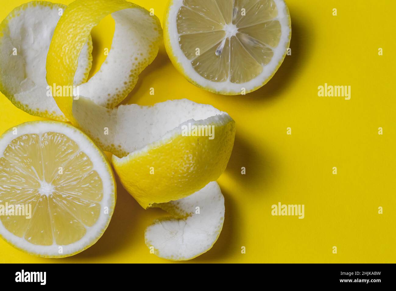 Fröhlicher Hintergrund von halbierten Zitronen und spiralförmigen Zitronenschalen auf einem gelben Papierhintergrund mit viel Platz für etwas Text Stockfoto