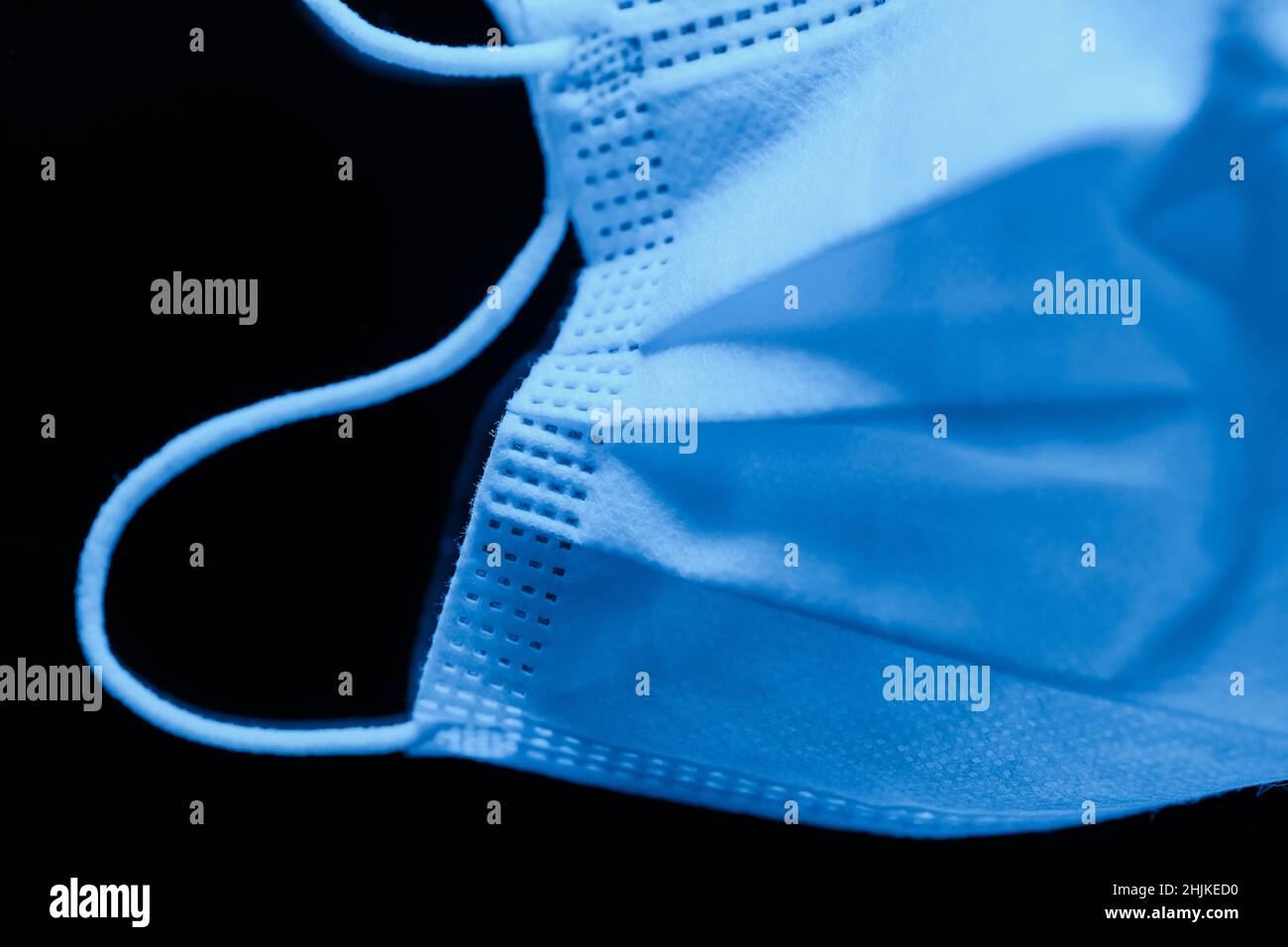 Chirurgische Maske in tiefen ultramarinen Tönen auf dunklem Hintergrund - Makroaufnahme Stockfoto