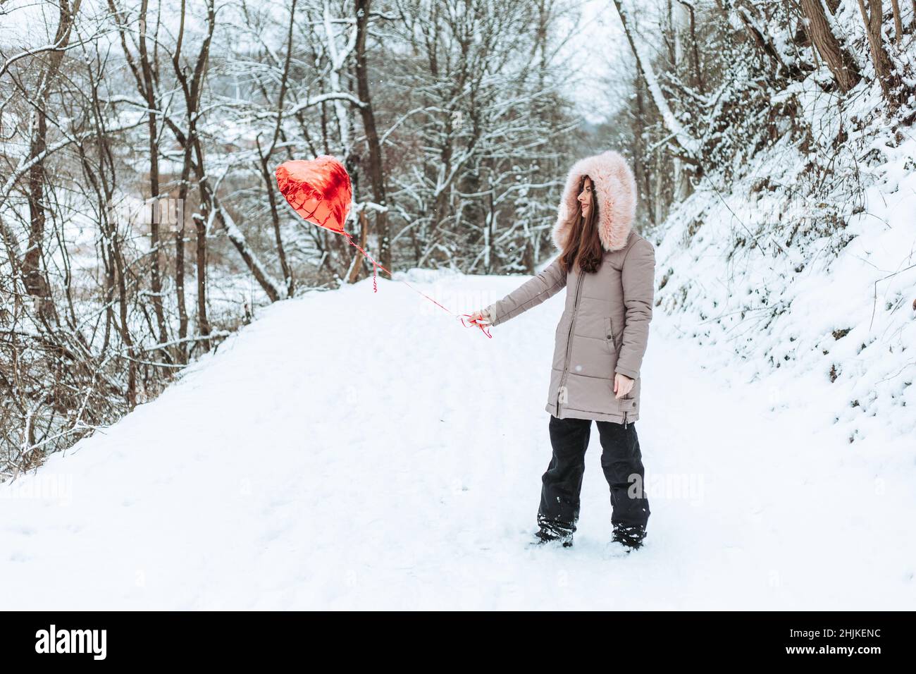 Mädchen steht auf der Straße im Wald mit einem roten Heliumballon Stockfoto