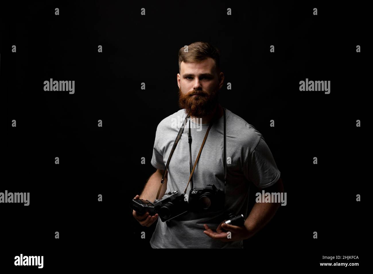Professioneller hübscher bärtiger männlicher Fotograf mit einer Reihe von Vintage-Fotokameras im Fotostudio, isoliert auf schwarzem Hintergrund. Stockfoto