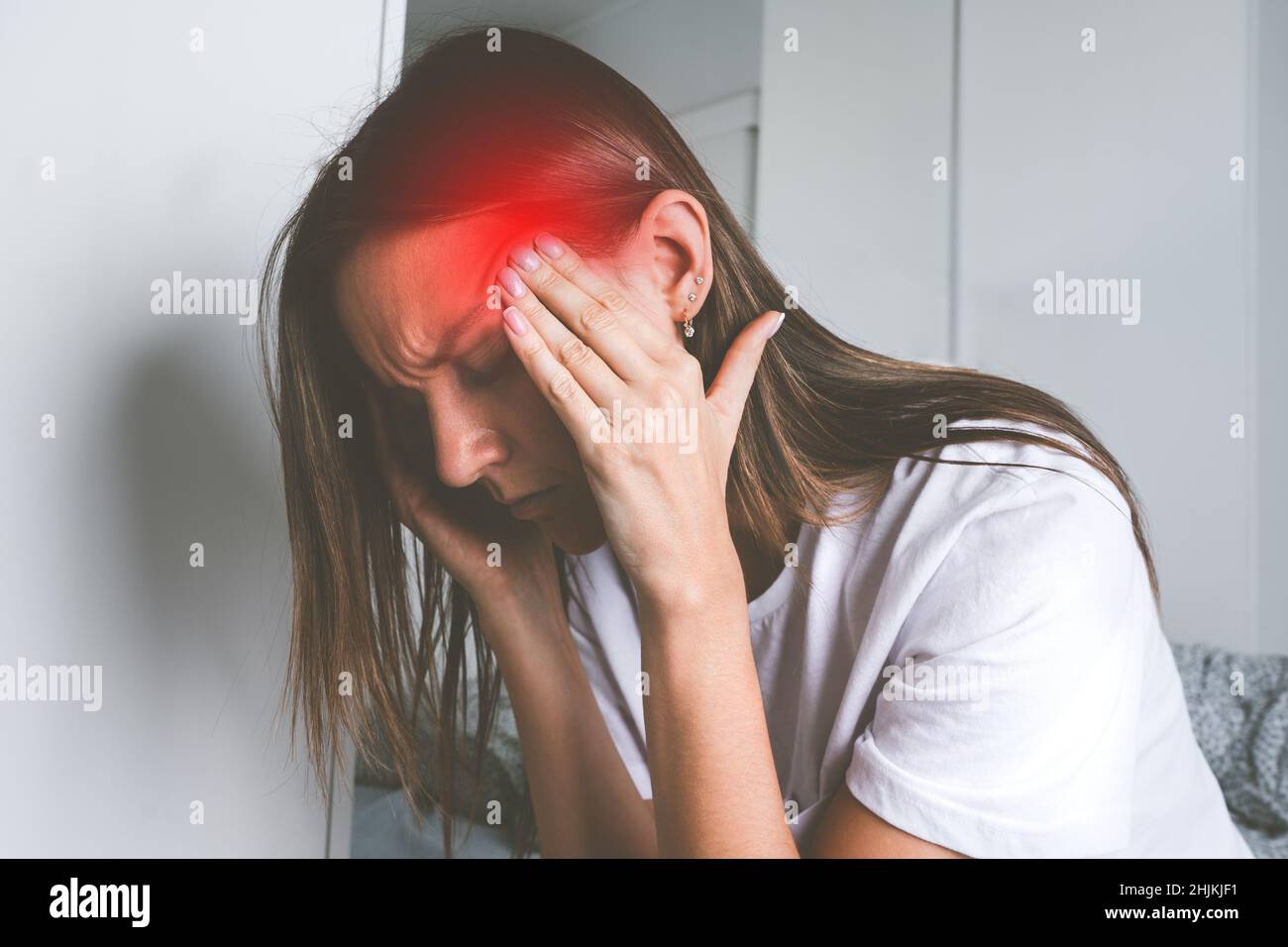 Junge Frau, die ihre Schläfe berührt und unter Kopfschmerzen, Kopfschmerzen oder Migräne leidet Stockfoto