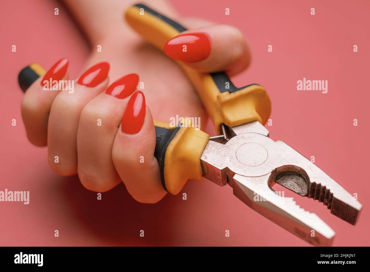 Nahaufnahme einer weiblichen Hand mit roter Maniküre und Zange. Stockfoto