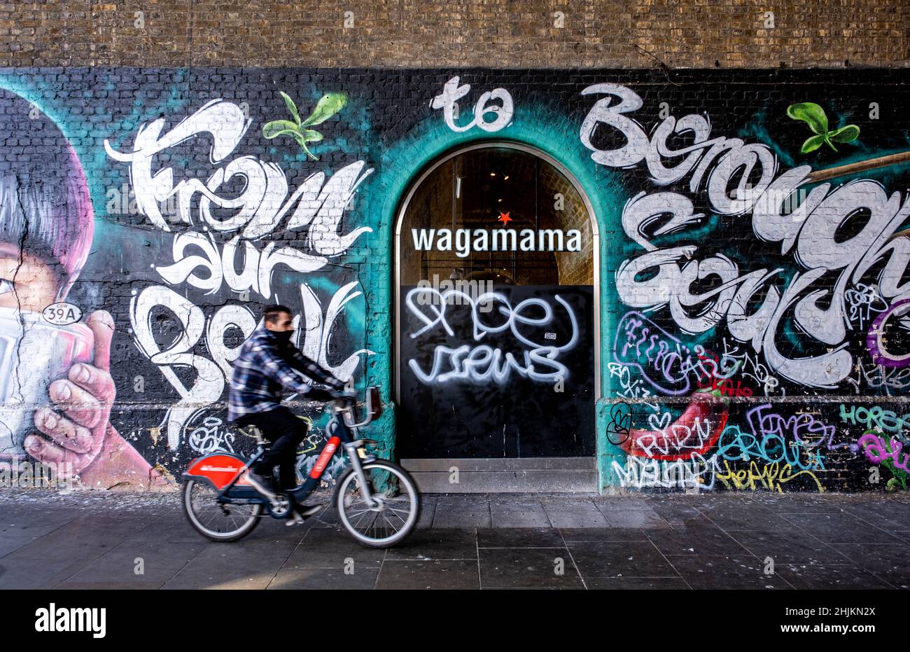 London England, 29. Januar 2022, Wall Art oder Graffiti vor Wagamama Restaurant Southwark Bankside mit Einem Mann auf dem Fahrrad vorbei Stockfoto